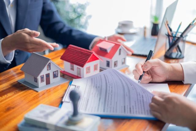 Person signing papers in front of model houses with someone behind those houses.