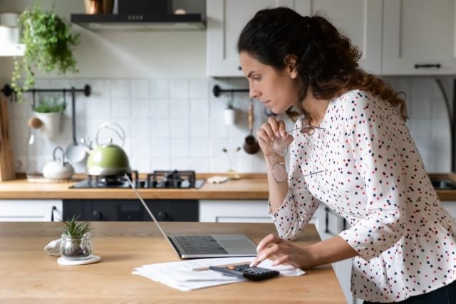 A woman looking at her laptop on a wooden counter.