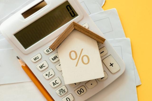 Wooden block shaped like house with a percent sign on the front on top of a calculator.