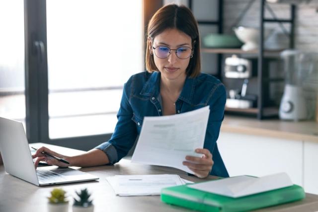 Woman reading over documents and using a laptop.