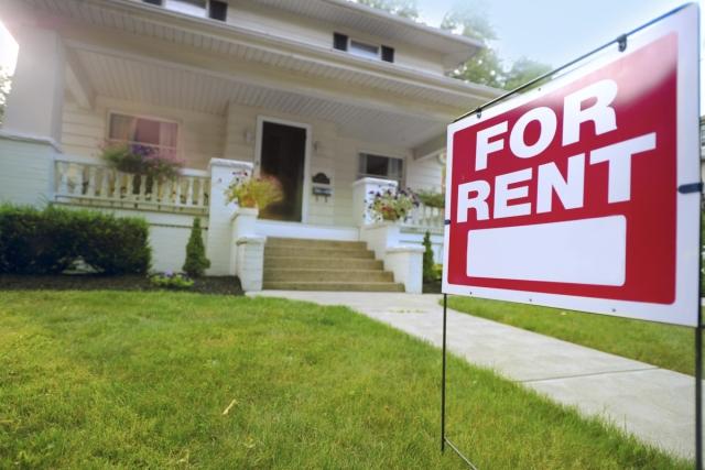 A red "For Rent" sign in the yard in front of a charming bungalow.