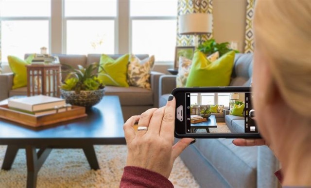 A woman taking a photo of a living room with her smartphone