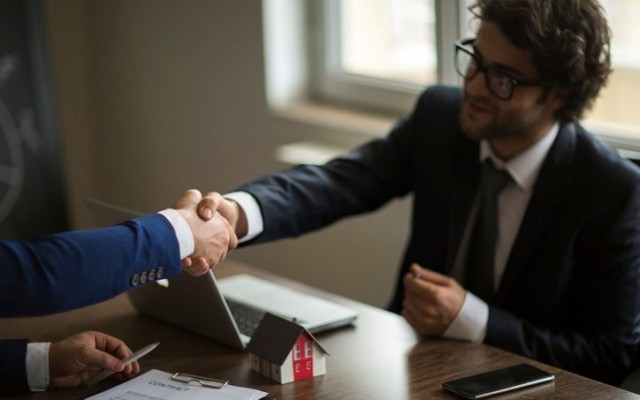 Person sitting at a table shaking hands after purchasing a property.