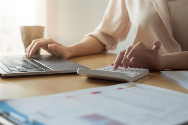 A woman types at a desk with an open laptop and calculator