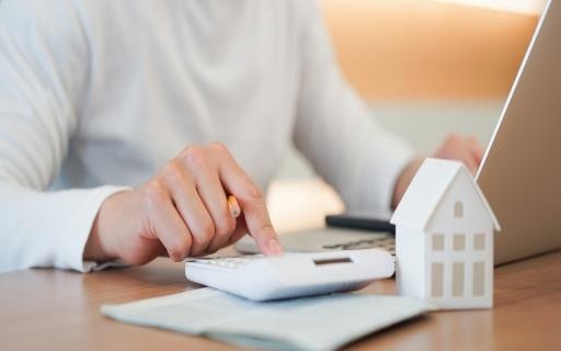 Person at laptop with a calculator and model of a house