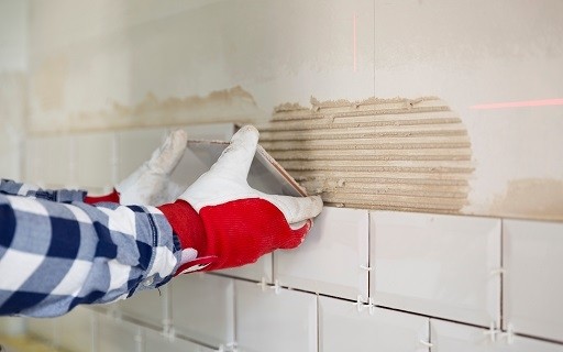 Gloved hands are in position to place a tile on building material on a wall