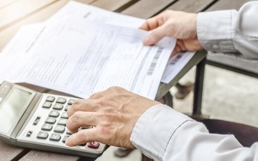 hands holding a copy of a pay stub and entering numbers on a calculator