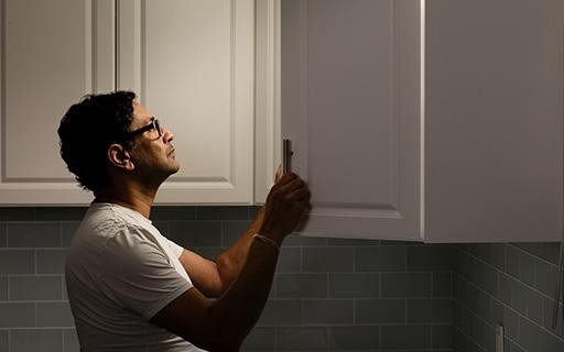 A man looks carefully into a kitchen cabinet