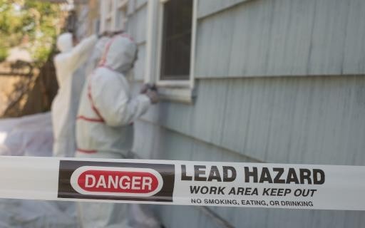 Caution tape for lead hazard with safety professionals and house in background