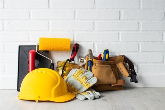 A collection of maintenance tools, including a hard hat, paint roller, and tool bag