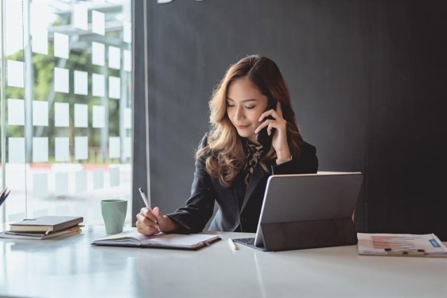 Office worker at desk on mobile phone, taking notes