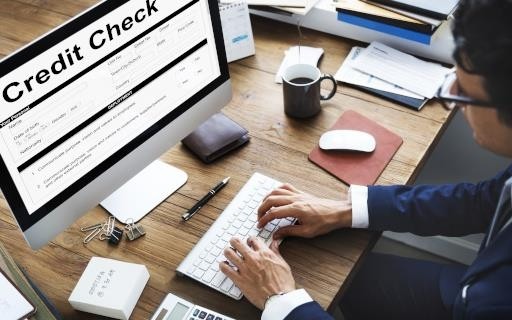 Image of a man at a slightly cluttered desk types on a keyboard with the words "credit check" enlarged at the top of the computer screen