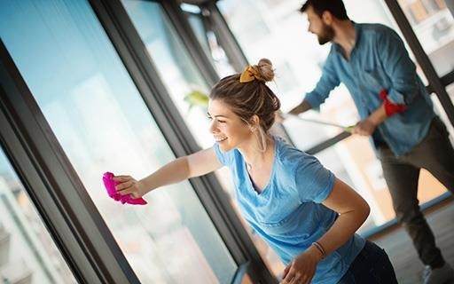 Woman and man cleaning floor to ceiling windows from inside