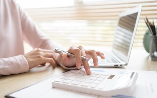 A close-up view of a landlord making calculations while looking at something on a laptop.