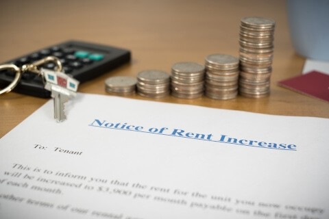 A pile of coins sits behind a notice of rent increase letter with a key laying on the corner.