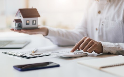 Person is tapping at a calculator with one hand while the other hands holds a model house.