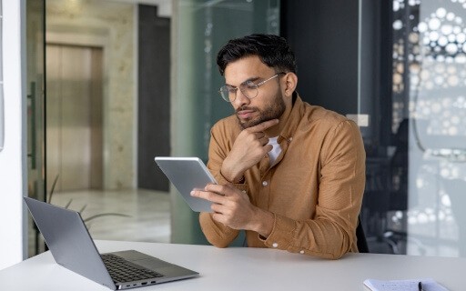 Man looking at tablet while laptop sits in front of him in an office.